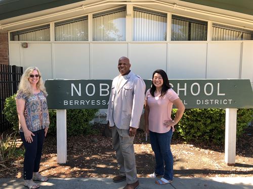 Three 4th grade teachers standing in front of a green Noble School sign
